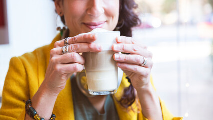 Unrecognizable smiling woman holding a cappuccino in her hands