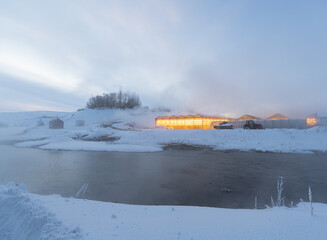 Iceland greenhouse with yellow light in a snowy landscape with steam from thermal baths on the banks of a river