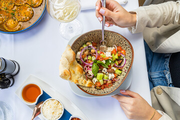 Mediterranean salad accompanied by a glass of white wine. Woman's hands eating salad