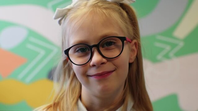 Portrait of Caucasian cheerful schoolgirl with glasses standing at school on the background of the wall with numbers. smiling, looking and laughing to camera. little girl elementary school pupil