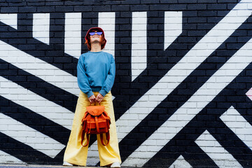 Hipster fashion young woman in bright clothes, sun glasses, bucket hat and backpack bag posing on...