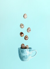 Easter minimal creative card. Quail eggs and falling to blue cup on light blue background. Top view.