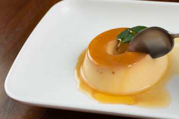 closeup milk pudding dessert, drizzled with whiskey, spoon and hand of the model in the photo,...