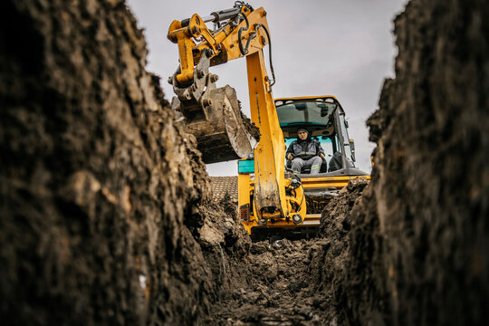A worker in bulldozer is moving soil and making hole on construction site.