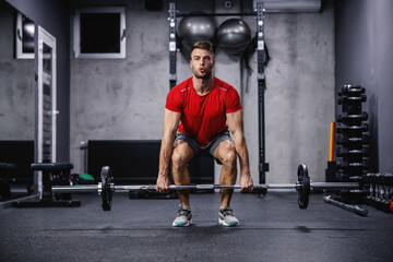 Fototapeta na wymiar Confidence and powerful movement, commitment to sports. Strong man in sportswear does an exercise, lifting barbell in a modern gym concept. Healthy lifestyle, stay in good shape, sports life