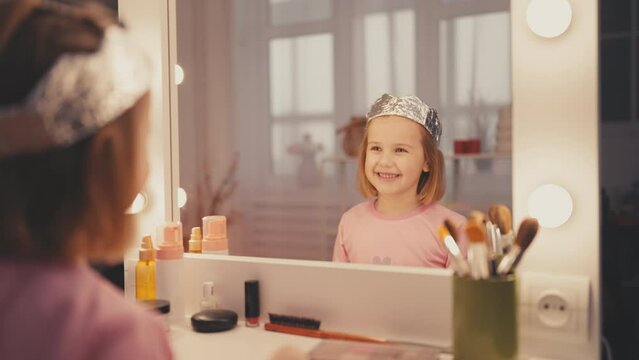Little girl wearing foil crown, having fun in front of mirror, happy childhood