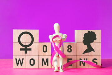 International Women's Day concept with wooden blocks and doll holding a purple ribbon