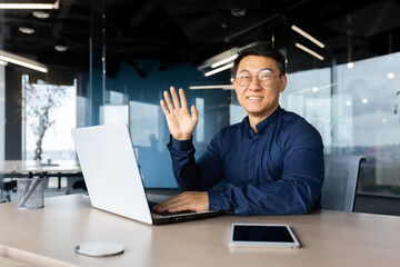 Portrait of a young handsome Asian male programmer working in the office at a laptop. Confidently smiling and looking at the camera.