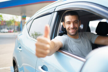 Happy cheerful Asian male car driver waving or showing thumb up and smiling out of the car. Happy man waves a hand and smiles to camera close up with copyspace. Safety driving and insurance concept.