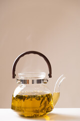 Green Chinese tea with orange zest in a glass teapot on a beige background