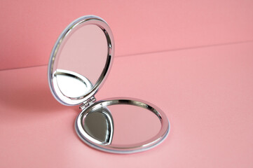 Cosmetic mirror on a pink background. Open round two-way mirror. Personal women's accessory.