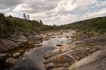 Serene view of the river flowing across the forest and rocky hills. Beautiful sky and clouds reflection in the water surface.