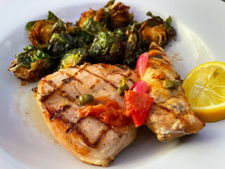 Close-up of grilled chicken with raosted brussel sprouts, lemon, and capers.