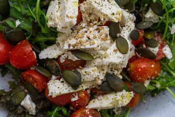 Salad with rucola, feta, cherry tomatoes, pumpkin seeds and sesame on a grey-blue handmade plate