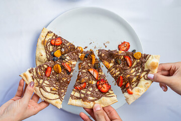 Woman's hand holding a piece of chocolate and strawberry pizza.