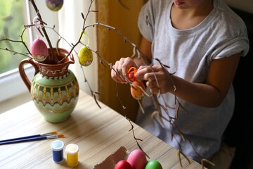 Fototapeta na wymiar A boy of seven years of Caucasian nationality, in the kitchen at home, paints Easter eggs, decorates a branch from a tree, is engaged in creativity