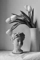 Biało-czarne zdjęcie kwiatów w wazonie i antycznej rzeźby. Kompozycja kwiatów i wyrzeźbionej...