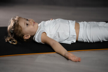 Little girl relax and meditate lying on the mat while practicing yoga in dark room
