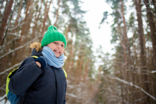 portrait of a smiling boy in warm clothes and with a backpack in a snowy winter outside