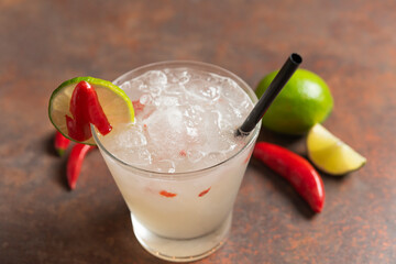 lime caipirinha with red pepper in glass cup on wooden surface