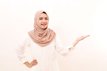 Portrait of happy young asian muslim woman standing while presenting something on blank space