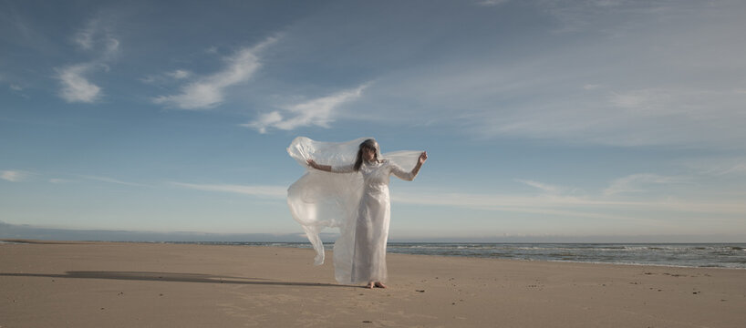 abstract art portrait of woman in white dress dancing on the beach holding transparent sheet of plastic foil
