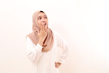 Surprised young asian muslim woman standing while covering her mouth and looking at blank space