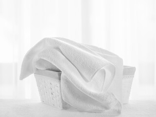 White towels in a gray basket against the background of a window with a white curtain in the bathroom
