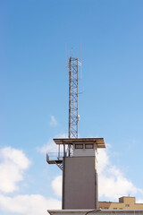 Wieża obserwacyjna z dużym masztem radiowym ( anteną) na płaskim dachu . Na tle błękitu nieba i chmur białych . - obrazy, fototapety, plakaty