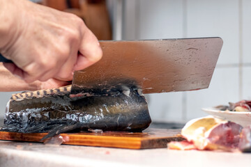 A woman cuts fish with a large knife at home in the kitchen