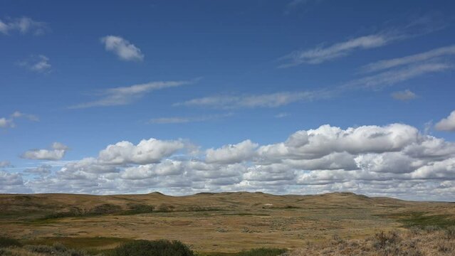 Time lapse of puffy white clouds in a blue sky above a dry landscape of small hills. 
