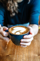 Cup of cappuccino in hand. Cup with hot coffee drink on the background of coffeeshop table. 