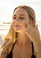 Caucasian blonde hair girl on the beach applying chemical free organic and vegan mineral sunscreen. Mention the beach, summer season with yellow and orange colors. Ocean waves with sun.