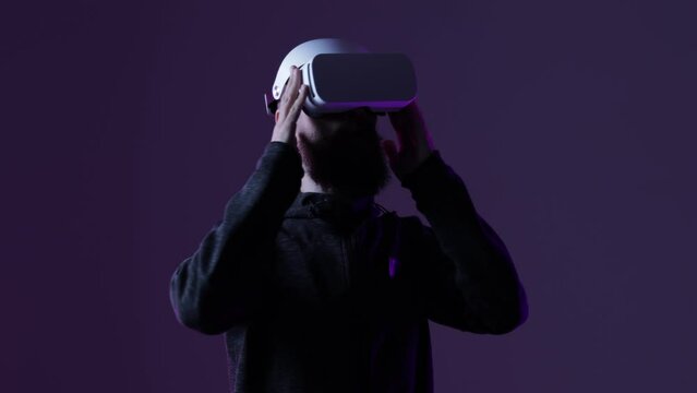 Young man in futuristic costume on dark background. Guy using VR helmet. Augmented reality, virtual reality, future technology, game concept. 