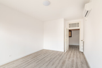 An empty spacious room for a bedroom, with an air conditioner and a radiator on the wall to create heat during the cold season. Eco wood floor.