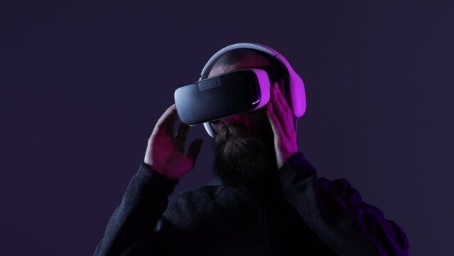Young man in futuristic costume on dark background. Guy using VR helmet. Augmented reality, virtual reality, future technology, game concept. 