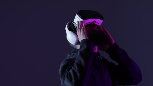 Young man in futuristic costume on dark background. Guy using VR helmet. Augmented reality, virtual reality, future technology, game concept. 