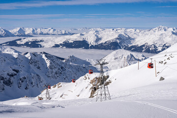 Red gondolas of cable car seen from Bellecote glacier, La Plagne ski resort, France,  in winter. Inversion clouds in valley