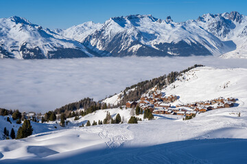 View of Plagne Soleil ski resort in French Savoy Alps. Snowcapped mountains, cloud inversion and apartment buildings - obrazy, fototapety, plakaty