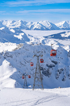 Red gondolas of cable car seen from Bellecote glacier, La Plagne ski resort, France,  in winter. Inversion clouds in valley
