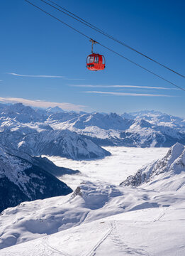 Red gondola of cable car seen from Bellecote glacier, La Plagne ski resort, France,  in winter. Inversion clouds in valley