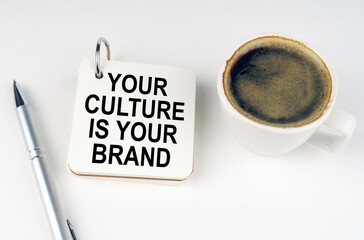 On a white surface, a cup of coffee, a pen and a notepad with the inscription - Your Culture is...