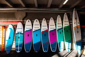 Colorful inflatable stand-up paddle boards SUP by the wall. Surfing and sup boarding equipment close up