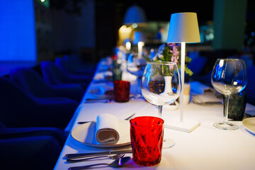 a table with a white tablecloth, glasses, crockery and decor in dark restaurant