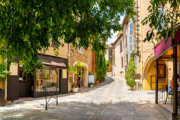 A shady treelined and hilly street or alley of shops and homes in the medieval hilltop village old town of Grimaud, France, in the Provence Cote d'Azur region.