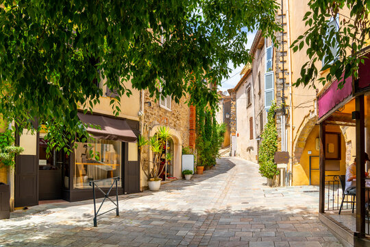 Fototapeta A shady treelined and hilly street or alley of shops and homes in the medieval hilltop village old town of Grimaud, France, in the Provence Cote d'Azur region.