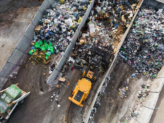 Wheeled loader loading bucket with garbage material and moving it, doing waste management tasks at a landfill, drone view