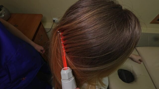 Professional beautician doing darsonval hair treatment procedure for young woman in beauty salon. High quality 4k footage