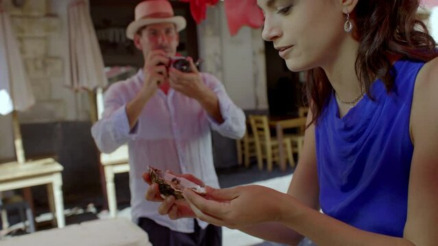 couple eating raw oysters in catania street fish market and taking pictures with camera