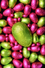 Pile or group of multi colored and different sizes of colourful foil wrapped chocolate easter eggs in pink, and green, with a large lime green egg in the middle.